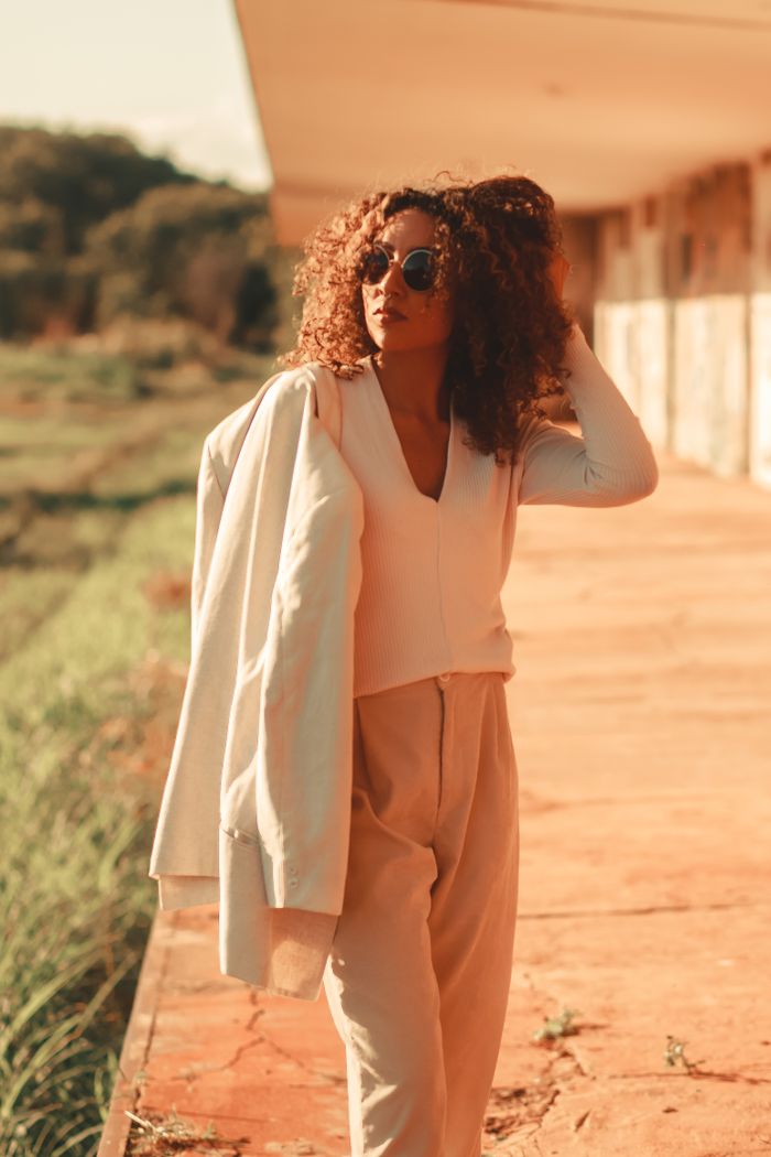 services-02 Trendy woman with curly hair poses in stylish outfit outdoors on a sunny day.
