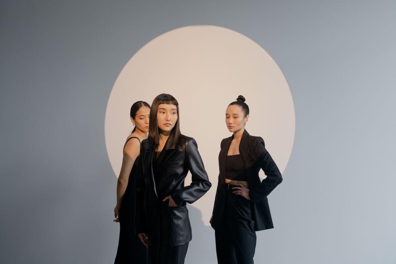 services-01 Three women in black clothing pose confidently in a minimalist fashion studio shoot.