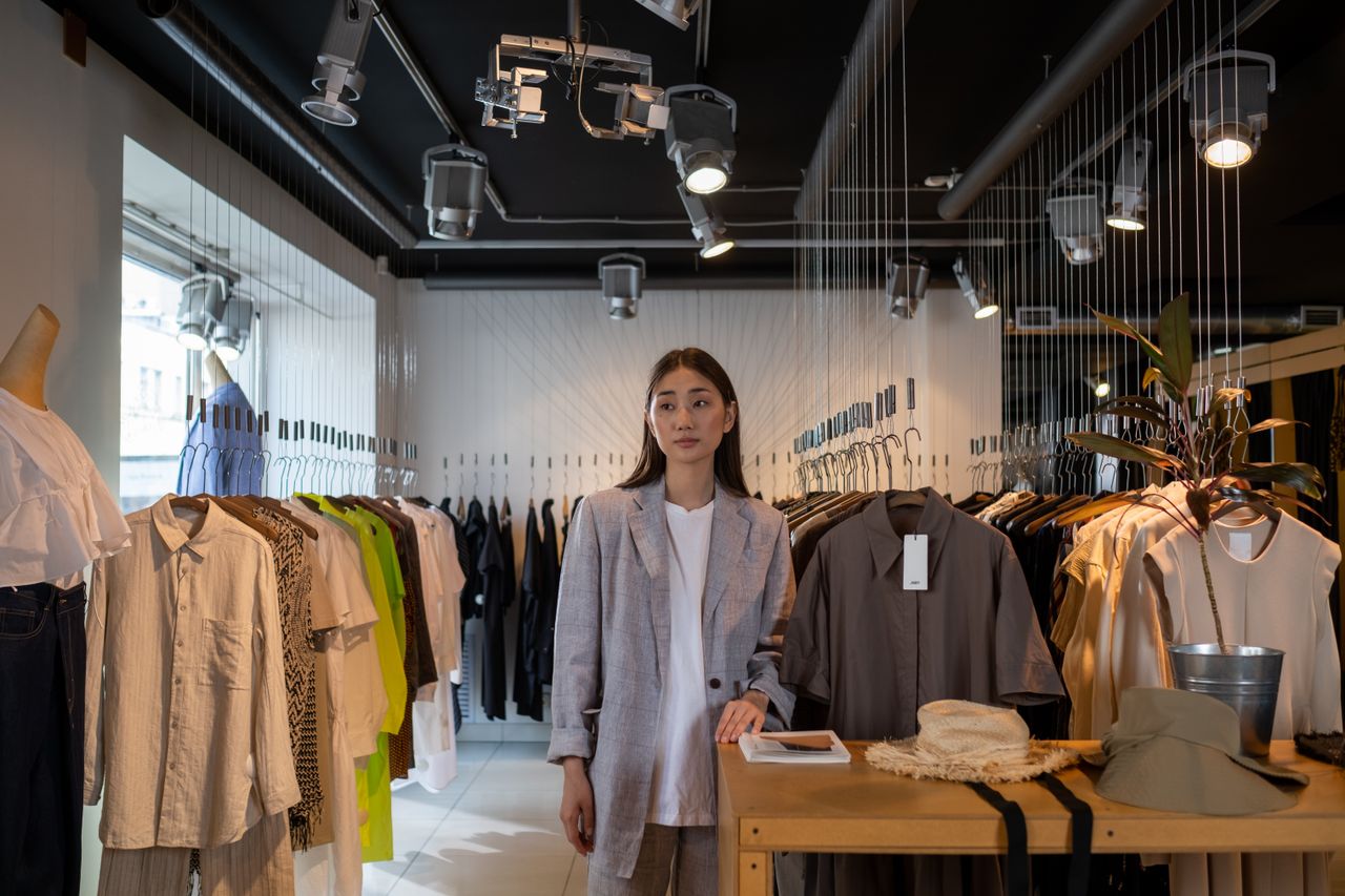 our-story Stylish Asian woman standing in a modern clothing boutique, showcasing contemporary fashion.