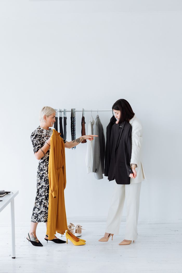 services-03 Two women discussing clothing choices in a minimalist boutique setting.